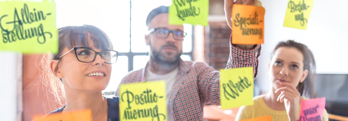 Personen beim Positionierungsworkshop vor Glaswand mit Zutaten für Markenpositionierung als Dienstleister in freien Berufen