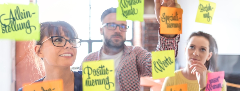 Personen beim Positionierungsworkshop vor Glaswand mit Zutaten für Markenpositionierung als Dienstleister in freien Berufen